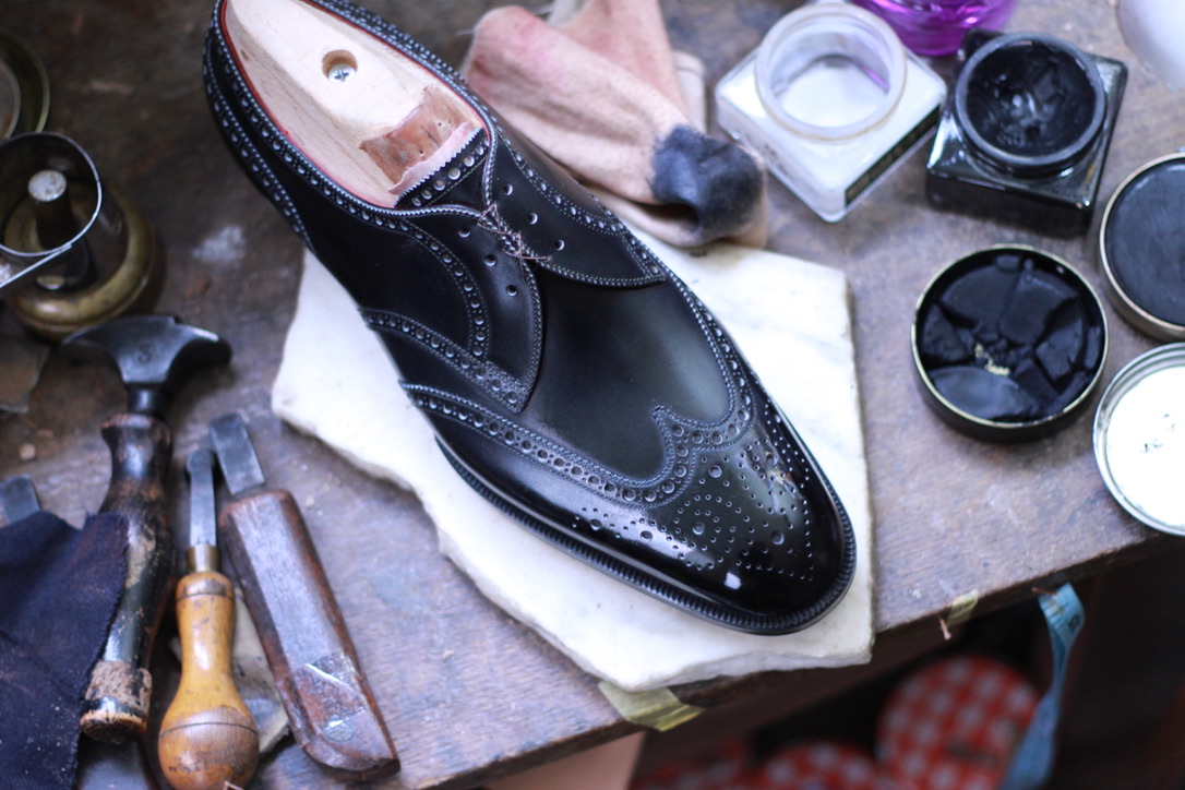 Black full-brogue bespoke shoe on the workbench with shoemaking tools